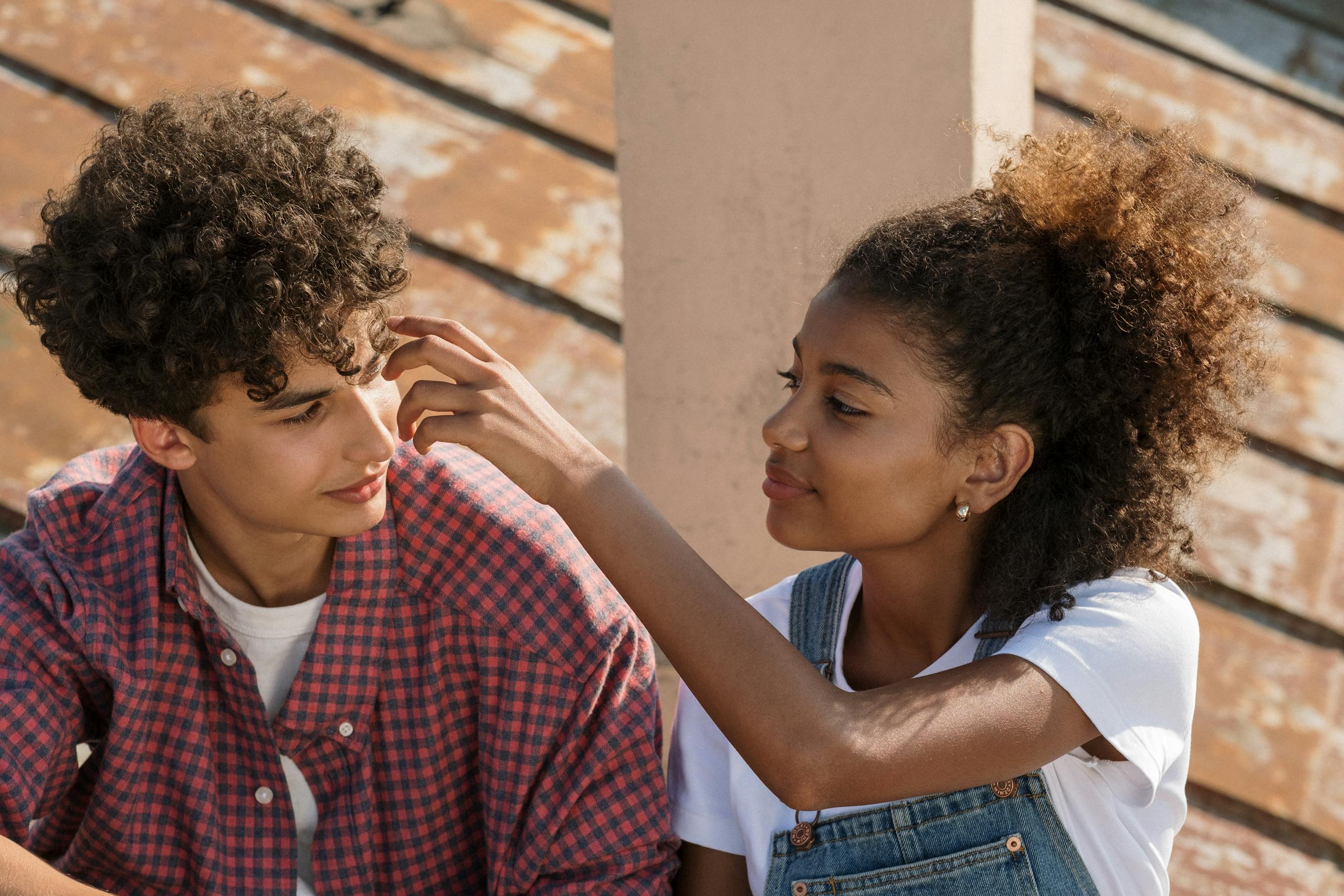 A young couple sharing an affectionate moment on a rooftop with a sunny backdrop.