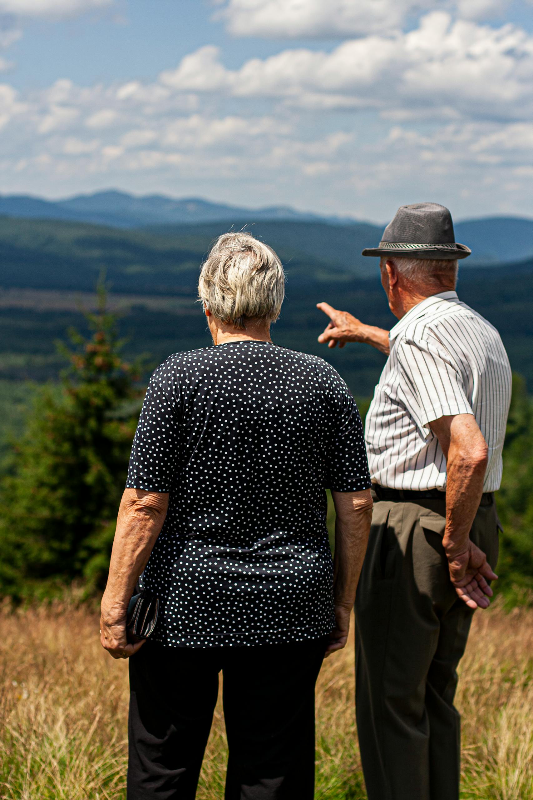 Senior couple standing together, admiring a stunning mountain landscape on a sunny day.